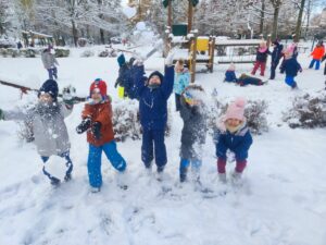 Grupa dzieci rzucająca śniegiem w ogrodzie przedszkolnym.