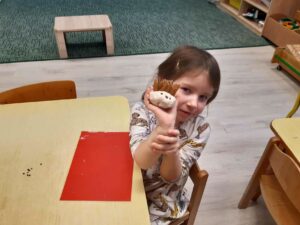 Dziewczynka siedząca przy stoliku, trzymająca w dłoni swojego jeża z masy solnej.
