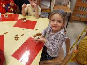 Dzieci siedzące przy stoliku i prezentujące wykonane jeże z masy solnej i makaronu.
