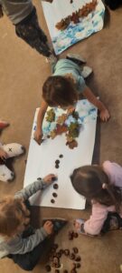 Grupa dzieci układa liście i kasztany na białym brystolu 