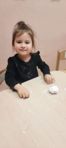Dziewczynka siedzi przy stoliku, przed nią kula ze sztucznego śniegu