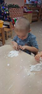 Chłopiec siedząc przy stoliku bawi się sztucznym śniegiem