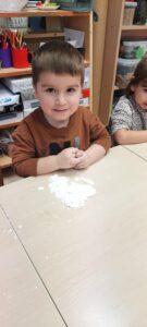 Chłopiec siedzi przy stoliku lepiąc ze sztucznego śniegu 