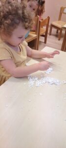 Dziewczynka siedząc przy stoliku bawi się sztucznym śniegiem