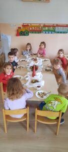 Grupa dzieci siedzi przy stoliku, na środku którego znajduje się świąteczna dekoracja 