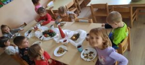 Grupa dzieci siedzi przy stoliku, na środku którego znajduje się świąteczna dekoracja