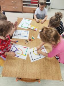 Grupa dzieci wyklejająca plasteliną kontury figur geometrycznych.