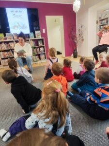 Przedszkolaki wysłuchujące opowiadania czytanego przez Panią bibliotekarkę.
