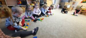 Grupa dzieci siedzi na dywanie, każde ma 6 kolorowych klocków 