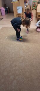 Dzieci stoją na dywanie, na stopie trzymają kostkę z kolorowych klocków 