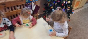 Grupa dzieci siedzi przy stoliku I maluje farbami bryłę lodu 