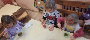 Grupa dzieci siedzi przy stoliku I maluje farbami bryłę lodu 
