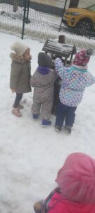 Grupa dzieci wsypuje ziarna do karmnika 