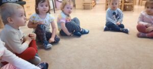 Grupa dzieci siedzi na dywanie poruszając buzią
