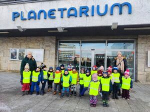 Grupa dzieci w kamizelkach odblaskowych wraz z nauczycielkami pod olsztyńskim planetarium