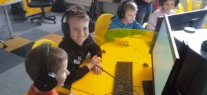 Dzieci w słuchawkach siedzą przy żółtym stoliku.