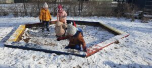Kilkoro dzieci bawi się śniegiem w piaskownicy 