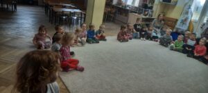 Grupa dzieci siedzi na dywanie 