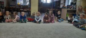 Grupa dzieci siedzi na dywanie 