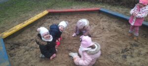 Pięcioro dzieci bawi się piaskiem w piaskownicy 