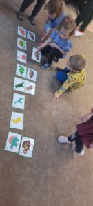 Dzieci stoją na dywanie kładąc szkielet dinozaura pod obrazkiem dinozaura 