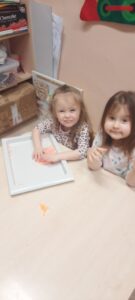 Dwie dziewczynki siedzą przy stoliku, przed nimi tacka z kolorową masą