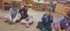 Czworo dzieci siedzi na dywanie prezentując konstrukcję z klocków 