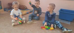 Troje dzieci siedzi na dywanie prezentując konstrukcję z klocków 