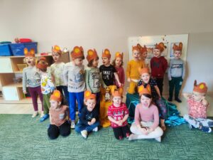 Grupa dzieci z brązowymi opaskami na głowie. Pomiędzy nimi maskotka Misia Uszatka.
