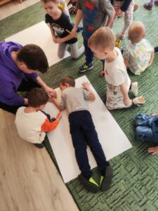 Dzieci odrysowujący postać chłopca na dużym arkuszu papieru.