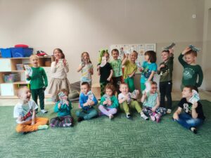 Grupa dzieci ubrana na zielono trzymająca kolorowe skarpetki z włóczki i tektury.