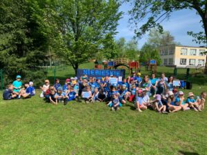 Grupa dzieci siedzących na trawie w niebieskich strojach sportowych.