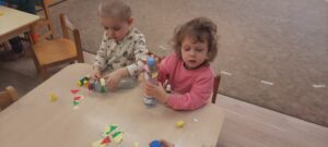 Dzieci siedzą przy stoliku naklejając kolorowe karteczki na plastikową butelkę 