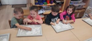 Dzieci siedzą przy stoliku bawiąc się sztucznym śniegiem 