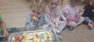 Dzieci siedzą na dywanie smakując owoc