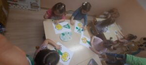 Dzieci siedzą przy stoliku wyklejając obrazek cebuli 
