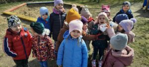 Grupa dzieci stoi w ogrodzie przedszkolnym trzymając koszyk z jajkami czekoladowymi 
