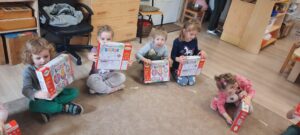 Dzieci siedzą na dywanie trzymając w dłoniach kolorowe pudełka 