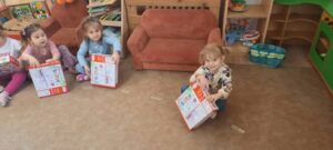 Dzieci siedzą na dywanie trzymając w dłoniach kolorowe pudełka 