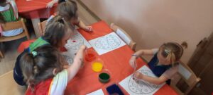 Dzieci siedzą przy stoliku, przy pomocy pipet malują pisankę 