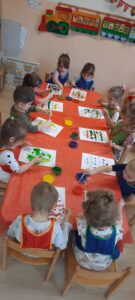 Dzieci siedzą przy stoliku, przy pomocy pipet malują pisankę