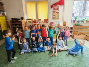 Grupa dzieci w sali przedszkolnej trzymająca marchewki w ręku.