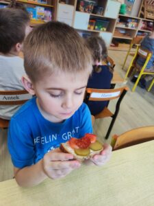 Chłopiec jedzący kanapkę z ogórkiem i pomidorem.
