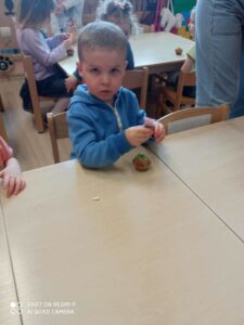 Dziecko siedzi przy stoliku dekorując pisakiem babeczkę