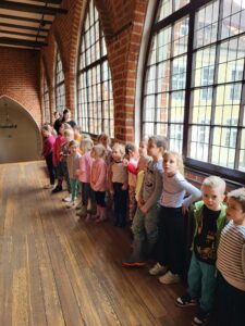 Grupa dzieci stoi przy oknach na zamkowym korytarzu