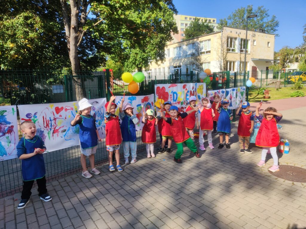 grupa dzieci z fartuszkach przed pomalowanymi plakatami