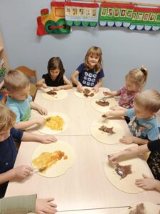 Kilkoro dzieci siedzi przy stoliku smarując dżemem i czekolada wafle 