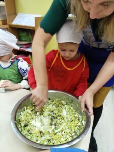 Dziewczynka razem z nauczycielką mieszą w misce składniki sałatki.