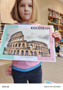 Dziewczynka trzyma w dłoniach ilustrację przedstawiającą koloseum