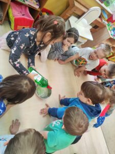 Grupa dzieci przygotowująca bańki. Dziewczynka wlewa do wody płyn do naczyń